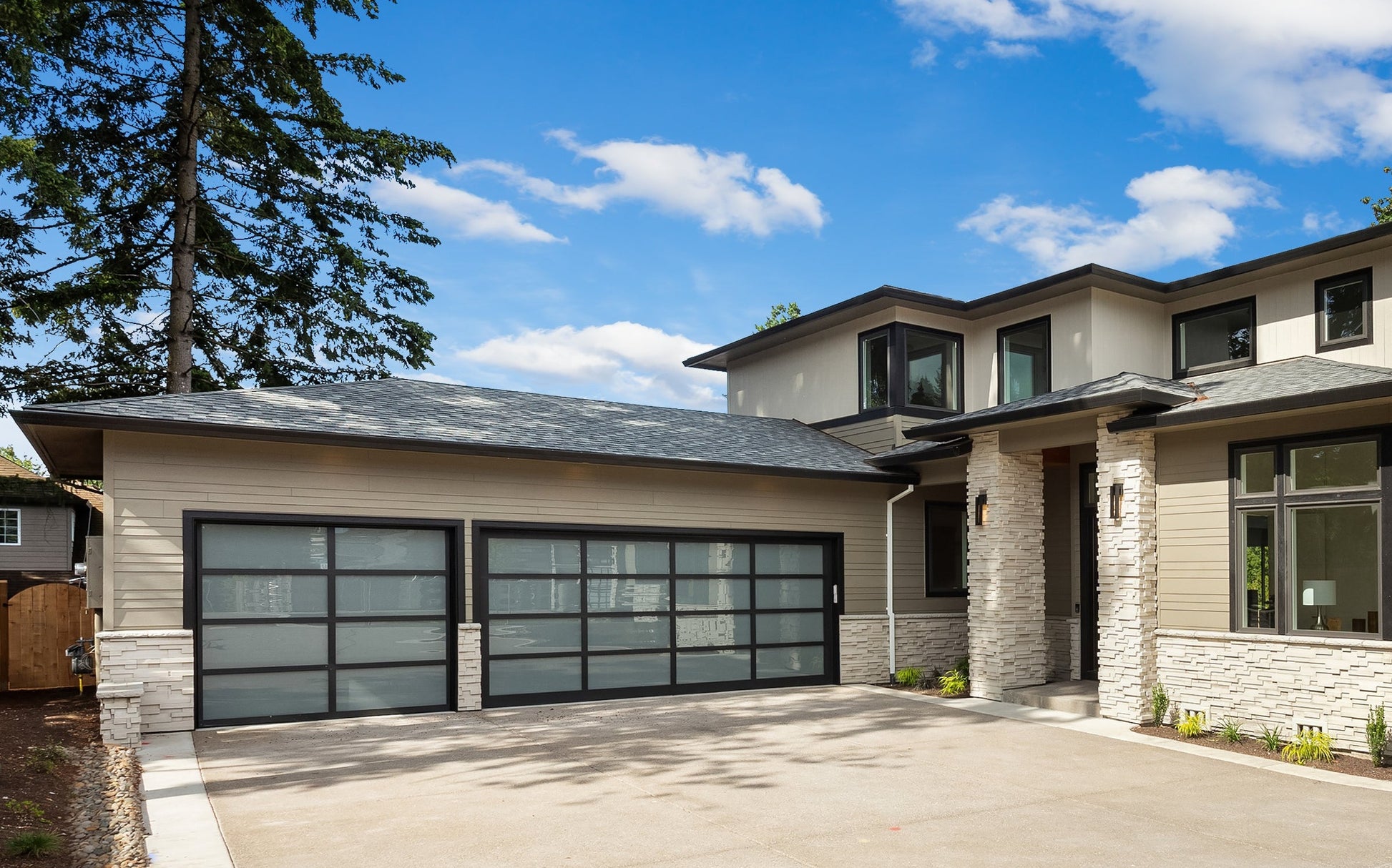 Bright daylight scene of a stylish modern home with matte black garage doors, surrounded by lush landscaping