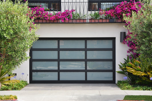 Chic modern garage door with matte black frame and frosted glass, set against a vibrant garden with flowering plants
