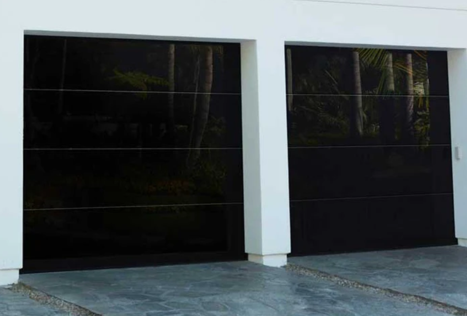 Close-up view of a sleek, frameless garage door with black-tinted tempered glass, enhancing a modern home's brick exterior. The door features a contemporary design, adding both style and sophistication to the property. Ideal for homeowners seeking a minimalist, elegant look.