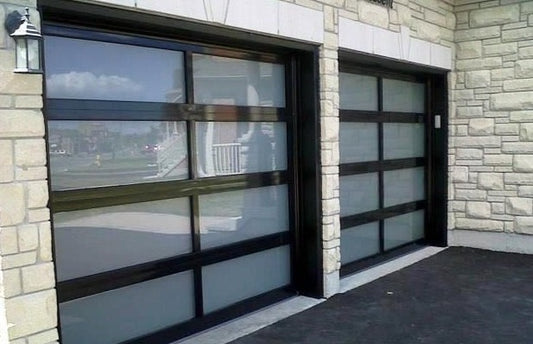 Stylish residential garage doors with matte black frames and large frosted glass panels, set against a natural stone building facade, enhancing the modern architectural design and curb appeal