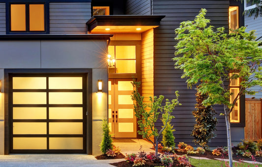 Modern house with a frosted glass garage door featuring a matte black frame, beautifully illuminated at dusk, highlighting contemporary architectural design and enhanced curb appeal