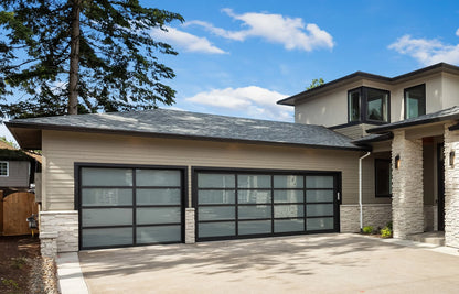 Bright daylight scene of a stylish modern home with matte black garage doors, surrounded by lush landscaping